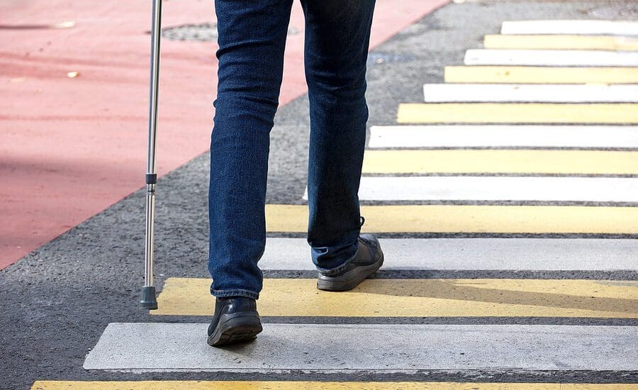 Man Walking With A Cane On Crosswalk. Male Legs In Jeans On Pede