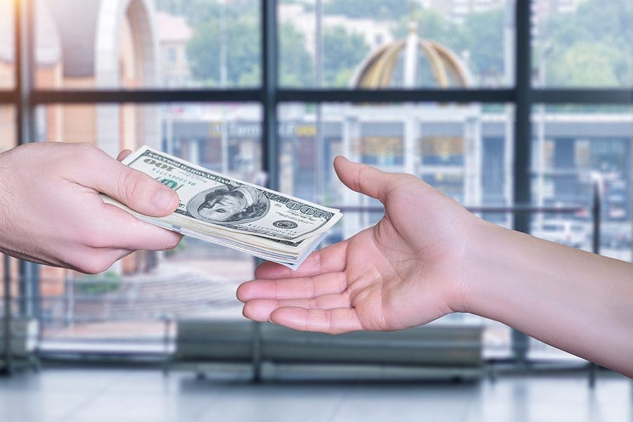 Money transfer concept. Businessman handing over money on a blurred background.