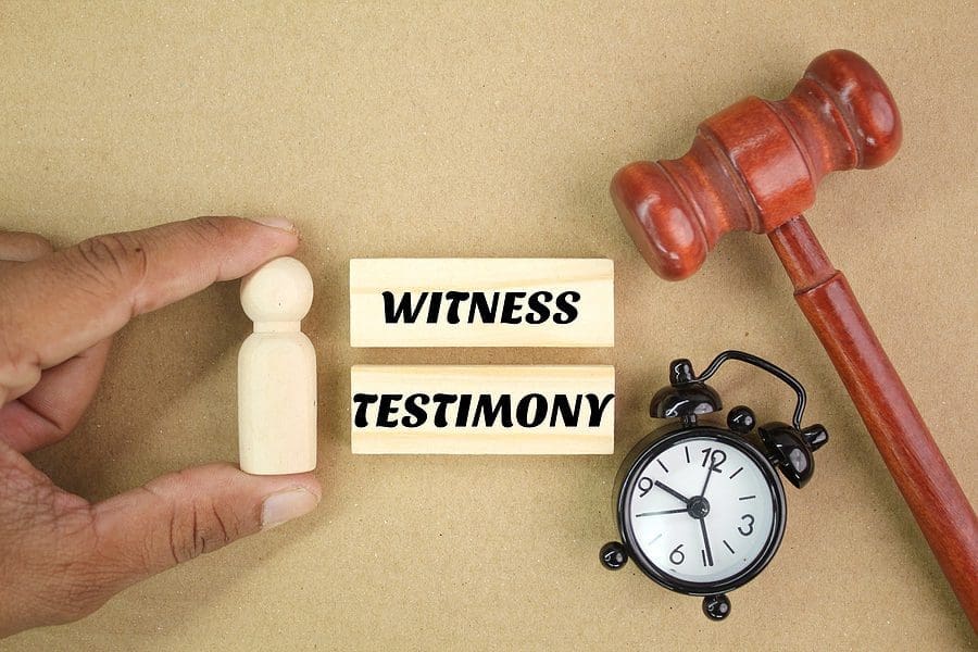 judge's gavel, wooden figure and bell clock with the words of witness testimony