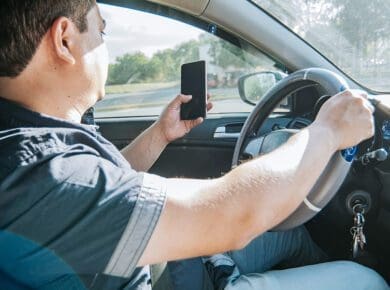 A man looking at a cell phone while driving the car, example of distractions that cause accidents