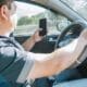 A man looking at a cell phone while driving the car, example of distractions that cause accidents