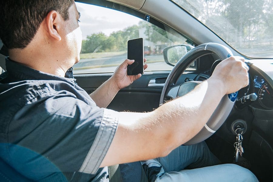 A man looking at a cell phone while driving the car, example of distractions that cause accidents