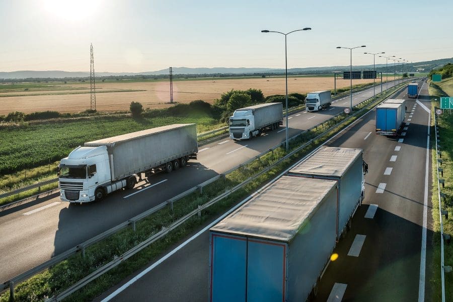 Transportation trucks in line passing on a highway on a bright blue day. Highway transit transportation with lorry trucks. Transportation And Trucking Industry.
