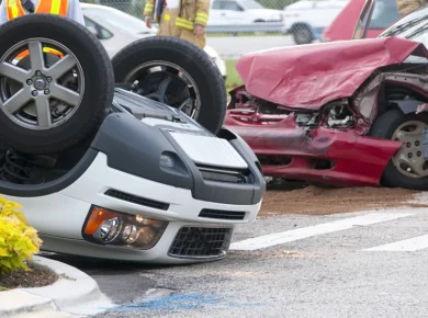 two cars, one overturned car and a red car with crushed hood after one of the major types of motor vehicle accidents