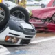 two cars, one overturned car and a red car with crushed hood after one of the major types of motor vehicle accidents