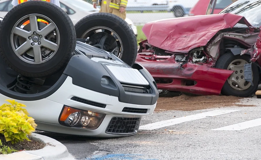 two cars, one overturned car and a red car with crushed hood after one of the major types of motor vehicle accidents