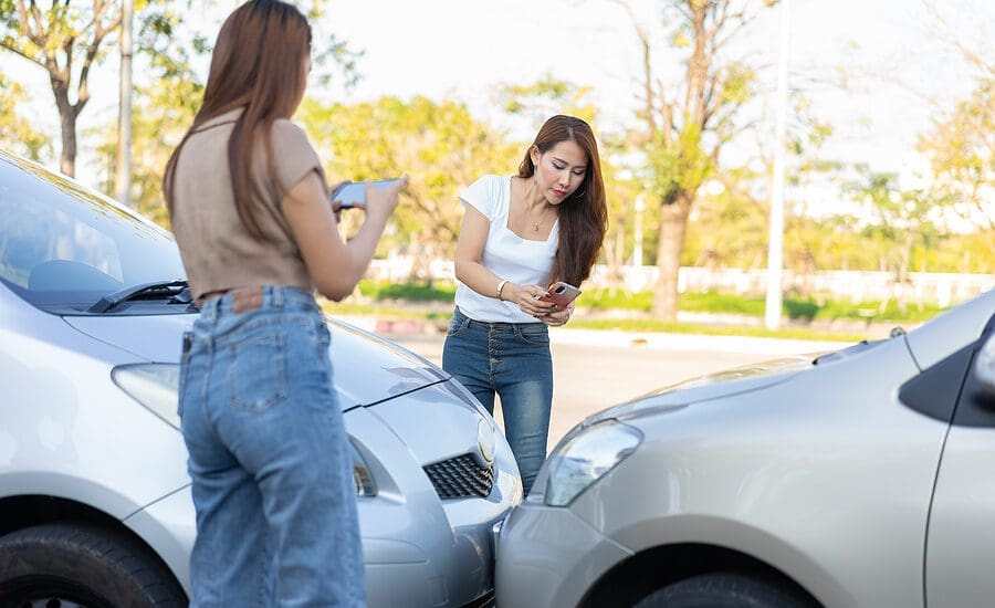 Two women use their phones to take pictures of where their cars collided head on