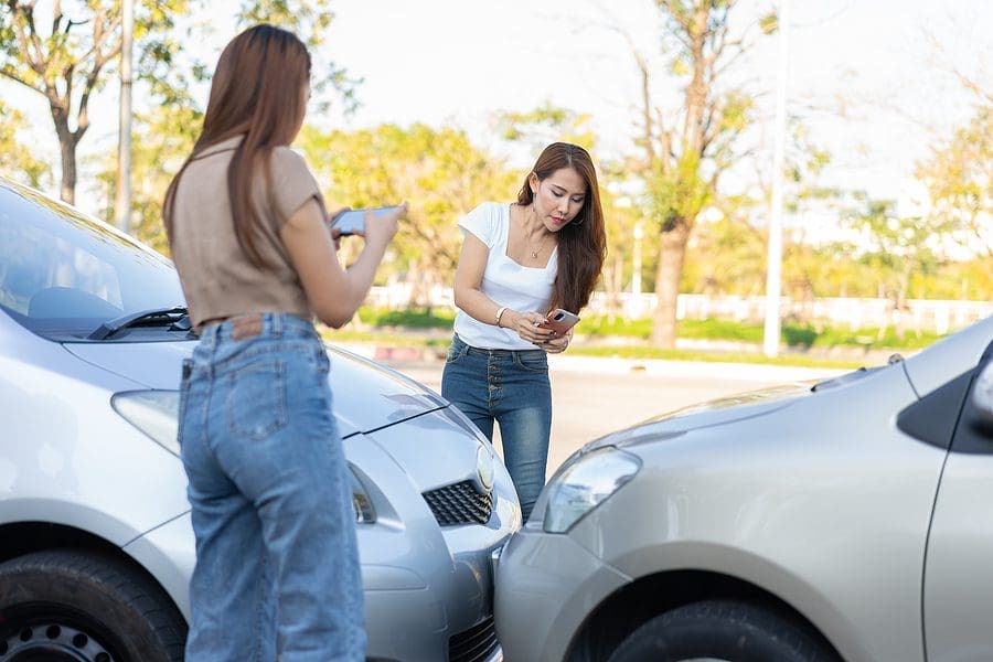 Two women use their phones to take pictures of where their cars collided head on