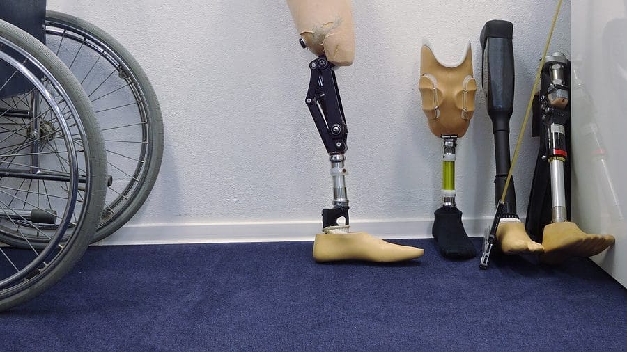 Four different types of prosthetic legs are lined up against a wall next to a wheelchair