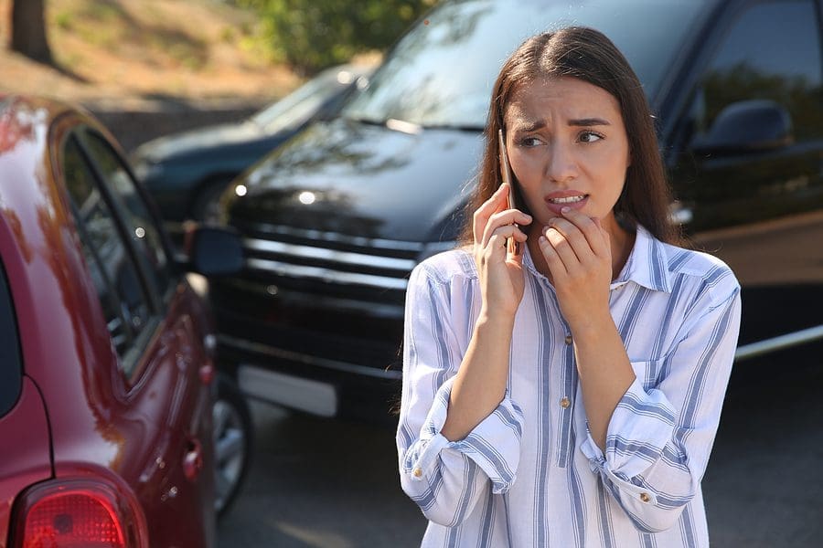 Woman talking on the phone at the the scene of a car accident looking stressed