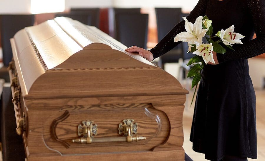 Woman holding white flowers placing her hand on a casket at a funeral