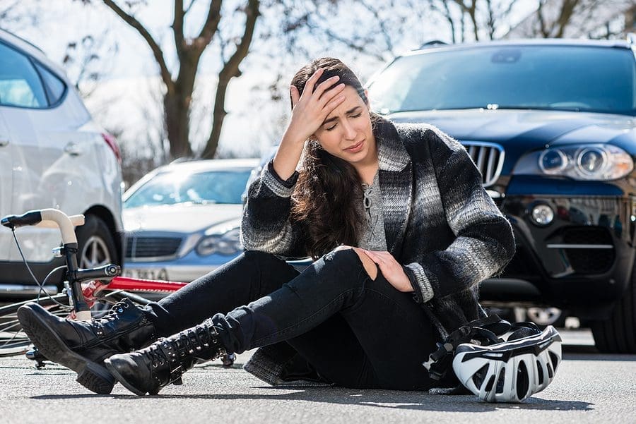 Injured woman sitting in the street holds her head after a bicycle accident involving a reckless driver