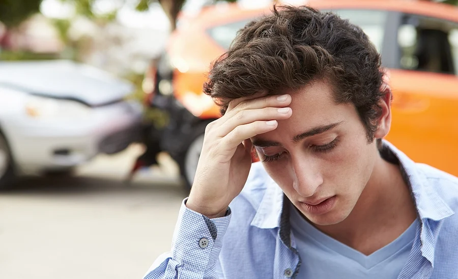 New teen driver stands in front of a car accident he caused looking worried