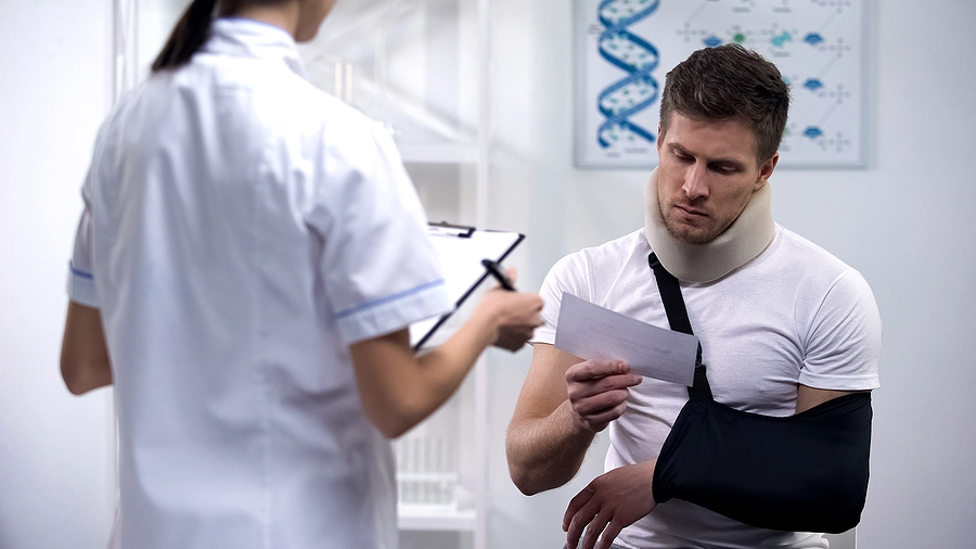 young man with his arm in a sling receives a bill from the doctor for treatment after a broadwater car accident