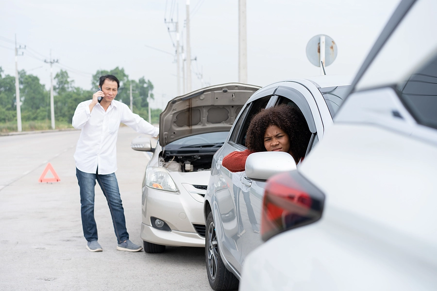 scene of an edgemoor car accident where an asian man is on the phone discussing the damage to his car and a black woman waits to exit the passenger side of the car he rear-ended