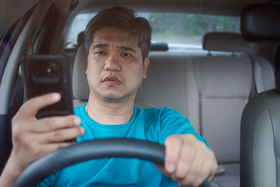 asian male driver texting while driving represents an example of negligence in an automobile accident
